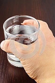 Hand holding glass of transparent purified water on wooden table