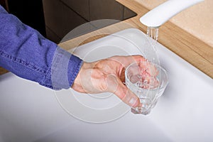 Hand holding a glass of water poured from the kitchen faucet