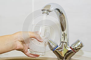 Hand holding a glass of water poured from the kitchen faucet