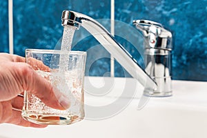 Hand holding a glass of water poured from a water tap