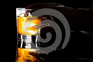 Hand holding a glass of whiskey on the rocks against dark background