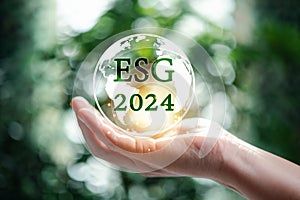 Hand holding globe with 2024 green ESG on nature background. 2024 Green business, environmental social governance sustainability.