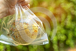 Hand holding globe inside plastic bag with green bokeh background using as climate change, recycle or environment and ecology