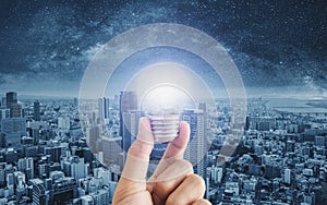 Hand holding glowing light bulb, with futuristic city background