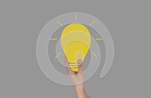 Hand holding glowing light bulb. Idea, inspiration, creativity concept on grey background.