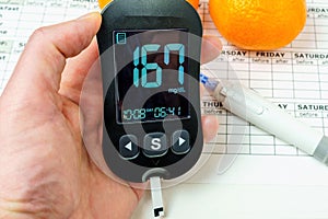 Hand holding a glucometer to determine the level of sugar in the blood. Concept of high blood glucose level. Table for recording