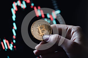 Hand holding a gold Bitcoin coin with candle stick graph chart and digital background