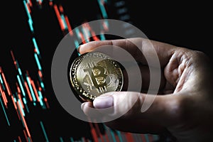 Hand holding a gold Bitcoin coin with candle stick graph chart and digital background