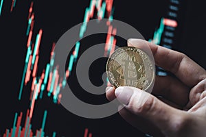 Hand holding a gold Bitcoin coin with candle stick graph chart and digital background