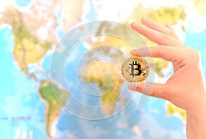 Hand holding gold coin of Bitcoin against map of world. Bitcoin