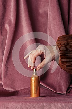 Hand holding golden perfume bottle on burgundy color fabric background