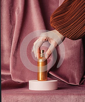 hand holding golden perfume bottle on burgundy color fabric background