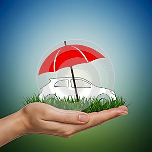 Hand holding grass patch with car silhouette and red umbrella, serene outdoor scene.