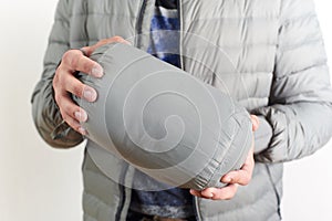 A hand holding a gray compression sack with a compact packable jacket or sleeping bag inside. Ideal for travel, camping