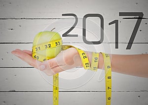 Hand holding green apple wrapped with measuring tape against 2017