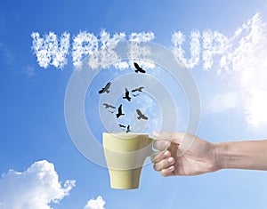 Hand holding green coffee cup with bird and wake up text on sky