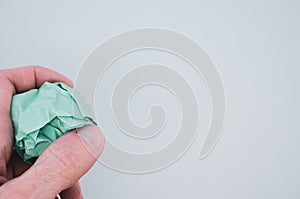 Hand holding a green crumpled paper ball on a light green background