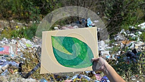 Hand holding green leaf painting on cardboard against open dumping, ecology