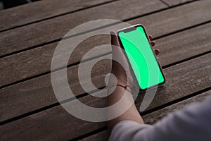 Hand holding green screen mobile phone on wooden cafe table at night