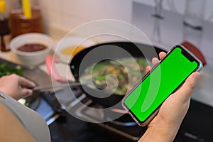 Hand holding green screen phone when cooking food in kitchen