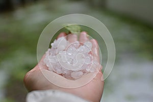 HAND HOLDING HAILSTONE AFTER A HAILSTORM IN A FIEL. DEFOCUSED BA