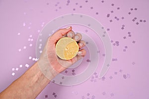 Hand holding half lemon on violet spa barkles ckground. Woman's handwith a piece of lemon. Top view, copy space photo