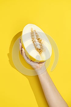 Hand holding half melon on yellow background