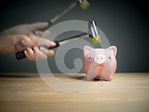 A hand holding a hammer which is raised above a pink sad piggy bank, with a shocked and apprehensive facial expression. photo