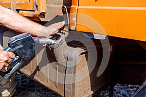 Hand holding handle fuel nozzle to refuel, petrol is pouring into the tank of an industrial mechanization