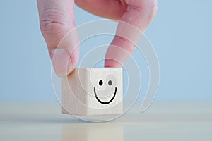 Hand holding happy face on wooden blocks. Emotion, Mental, Customer service evaluation and satisfaction survey concept.