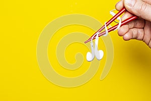 Hand  is holding a headphones using chopsticks on a bright yellow background, with copy space. Concept of musical taste