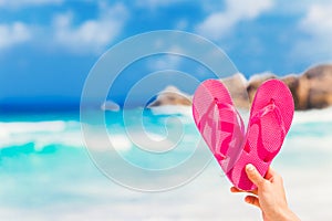 Hand holding heart shapes pink flip flops on a tropical sea resort background