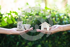 Hand holding home model change to money with green nature as ba