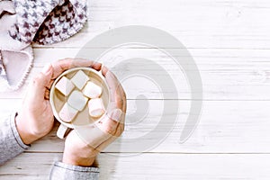 Hand holding hot chocolate and marshmallow on wooden background