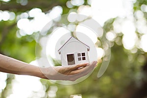 Hand holding house model to with green nature background