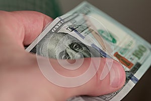 Hand holding a hundred dollar bill, showing the face of Benjamin Franklin. Extreme macro close up