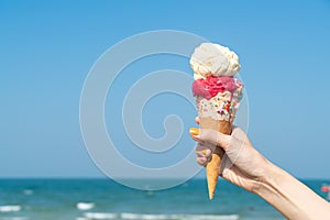 Hand holding ice cream cone with blue sky background