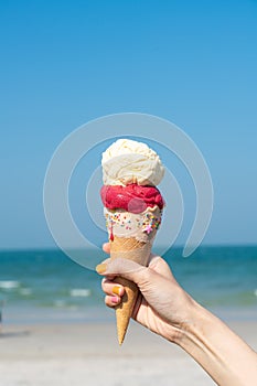 Hand holding ice cream cone with blue sky background