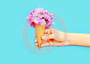 Hand holding ice cream cone with flowers over a blue background