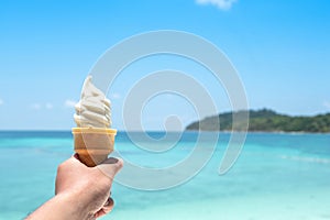 Hand holding ice cream or soft cream with blurred sea background
