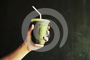 Hand holding Iced Green matcha tea mixed with ice cube and milk in latte glass dark background