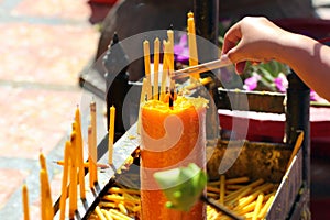 Hand holding incense sticks, lighting from the burning yellow candle. Traditional Thailand buddhist concept