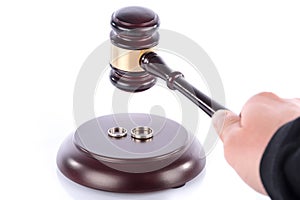 Hand holding a judge gavel above wedding rings