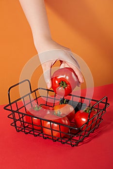 The hand is holding a juicy red tomato in a mesh basket. Orange and red background. Tomatoes are not only a healthy food but also