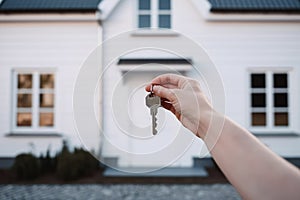 Hand holding a key on the background of the house. The concept of moving to a new place of residence