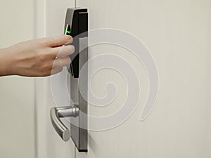 Hand holding key card in front of electronic lock to open white door room in hotel