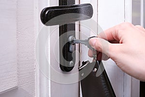 A hand holding a key and inserting it in a keyhole in order to open or lock a white wooden door, home security and protection