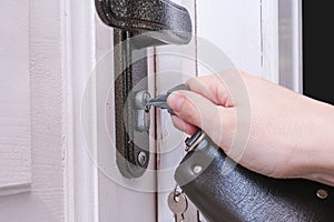 A hand holding a key and inserting it in a keyhole in order to open or lock a white wooden door, home security and protection