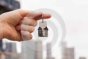 The hand holding a key to a dream house against the backdrop of the city skyscapes