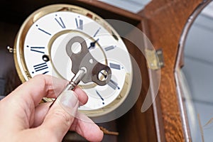 A hand holding a key to wind up a clockwork, vintage classic clock mechanism